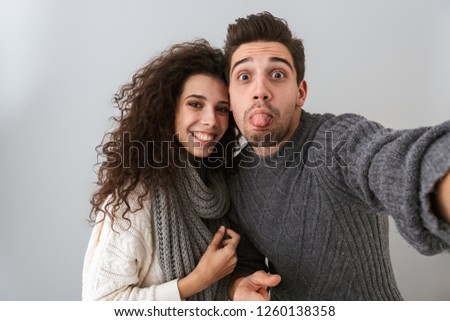Portrait of amusing man and woman taking selfie photo and gesturing with fingers isolated over gray background