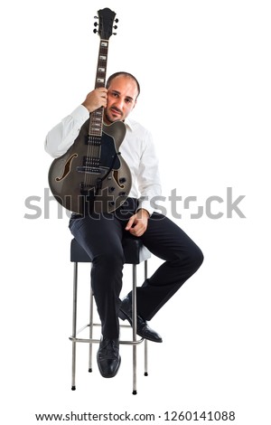 a well dressed jazz musician sitting on a stool and holding a guitar