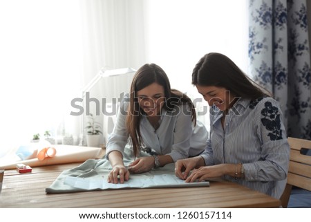 two beautiful women with long black hair work with a pattern and fabric, a concept of creativity and a hobby, a small business. Real home workshop