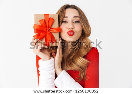 Image of a beautiful emotional woman in christmas costume holding present gift box blowing kisses.