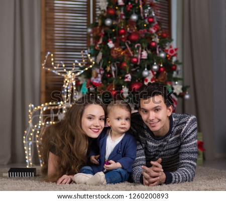 family sits with the baby sitting near the Christmas tree, the baby is one year old and a young woman and a man are waiting for Christmas