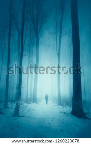 man walking on snowy road in forest on winter night