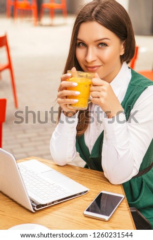 Brunette business woman working as a freelancer from a cafe in summer terrace. She drinks tea and use gadgets as laptop and tablet and phone for her work. Space for text