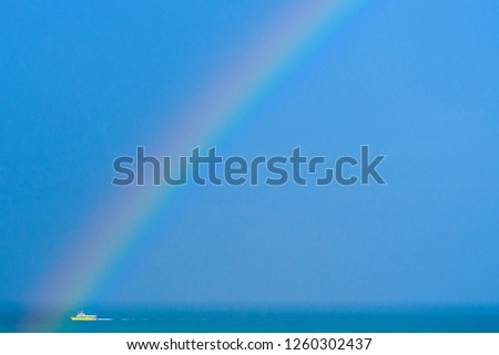 Rainbow over the sea while passing a boat in the distance