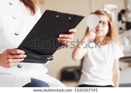 Eye health conception. Woman with documents tests the visual acuity of little girl.