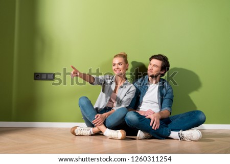 handsome man sitting on floor with attractive girl pointing with finger in apartment