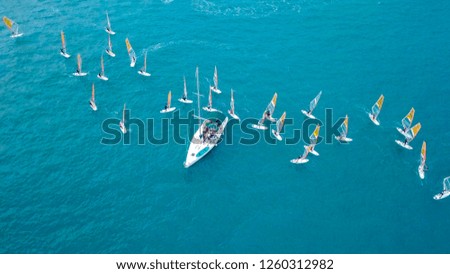 Small white yacht surrounded by a large group of Wind surfers at The Mediterranean Sea - Top down aerial image.