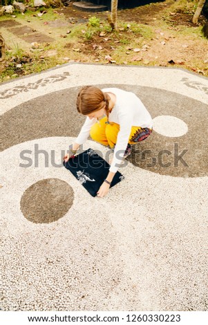 Young woman practicing yoga - meditation in the tropical garden with yin yang sign.