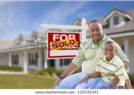 African American Father and Son In Front of Sold For Sale Real Estate Sign and New House.