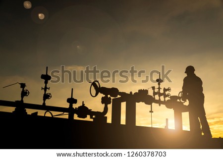 Silhouette of the oilfield worker monitoring the manifold valves in the oilfield  Royalty-Free Stock Photo #1260378703