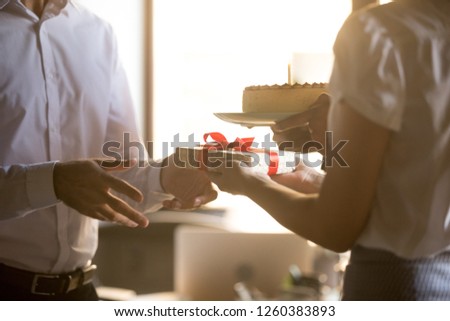 Colleagues greeting congratulating coworker receiving gift box and birthday cake, friendly employees make surprise giving presents to office worker, corporate party celebration concept, close up view