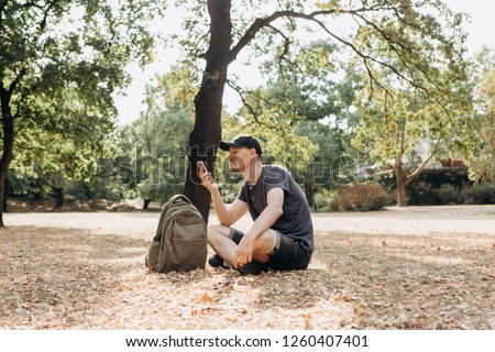 A guy with a backpack or a student sits in an autumn park and uses a mobile phone.