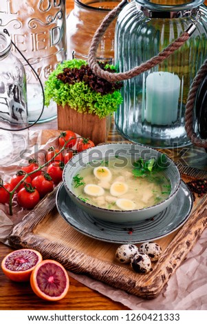 chicken broth with quail eggs in a gray plate on a wooden board in a rustic composition