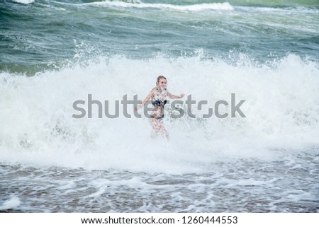 single happy young woman in swimsuit walking at sea surf with splashes