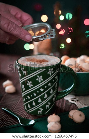Coffee drink with meringues which pour cinnamon on the background of Christmas lights