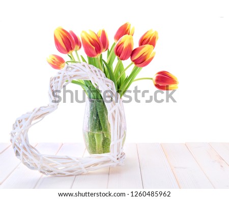 Spring decoration with red tulips and stugged heart on white wooden table, top part of the picture isolated on white background