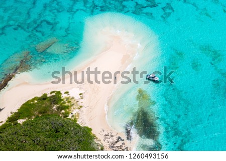 Tourists, divers, snorkelers, jet boat, an idyllic empty sandy beach of remote island, azure turquoise blue lagoon, West Coast barrier reef, aerial view. New Caledonia, Melanesia, South Pacific Ocean. Royalty-Free Stock Photo #1260493156
