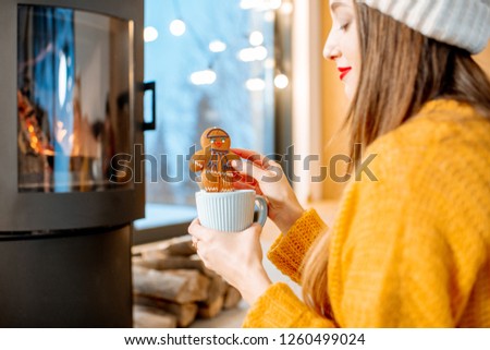 Woman holding Christmas gingerbread with cup near the fireplace at home