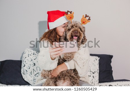 young woman at home. wearing a santa hat taking a selfie with her dog on bed. Indoors. Christmas concept