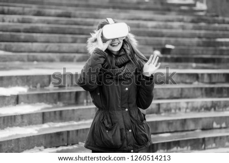 Pretty hipster young girl plays virtual reality mobile game app on smartphone attached to modern VR glasses outdoor in cold winter day