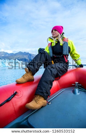 Woman is taking a boat trip to Jokulsarlon Glacier Lagoon in Iceland. The boat surrounded by icebergs. She wears windproof and waterproof suit and hiking boots
