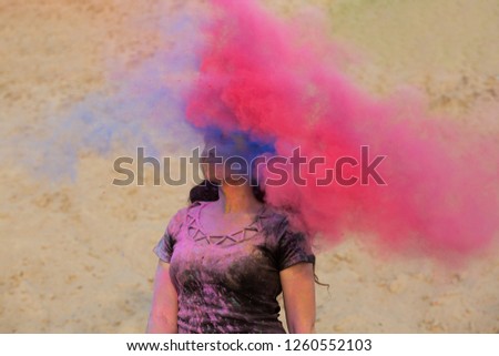 Pretty brunette model with long wavy hair having fun with pink and blue dry Holi powder at the desert
