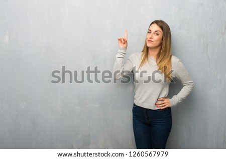 Young woman on textured wall showing and lifting a finger in sign of the best