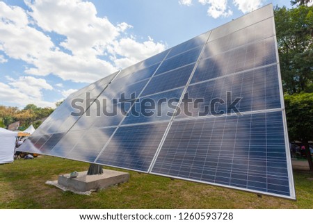 Alternative sun energy concept. Low angle top side view photo of solar panel element against green nature and clear blue sky