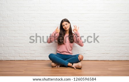 Teenager girl sitting on the floor in a room showing ok sign with and giving a thumb up gesture