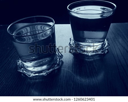 Cold water drinks. There are glass coasters. Both water drinks are transparent. Refreshing water beverages. Black and white picture. There is a black background.