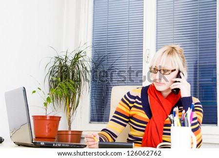 Young business woman speaking on mobile phone while using laptop at office