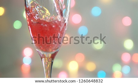 Pouring Sparkling Red Wine into a glass with pastel rainbow bokeh defocused lights background. Christmas and New Year celebrations theme, Holidays party concept. (selective focus, space for text)