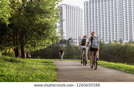 Two young cyclists are moving away on the road through the park and big white apartment buildings on the backround