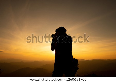 Silhouette Young men Travelers standing are Shooting photograph on the mountain There is a beautiful sunset as the background.