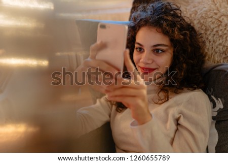 photo of beautiful young woman with curly hair is reading messages on her smartphone