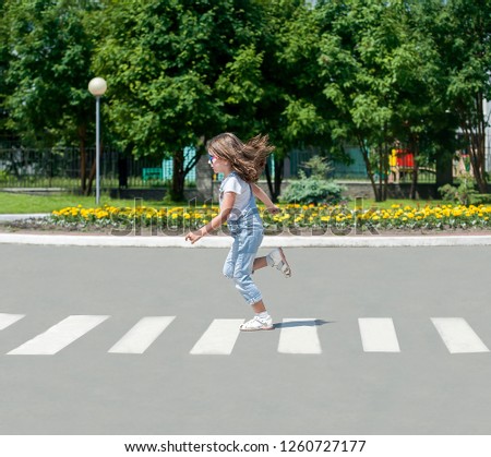 In the summer on the street at the pedestrian crossing kid girl in fashion clothes cross the road