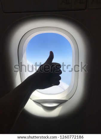 Silhouette of hand shows the thumb up, sitting in the plane at window.