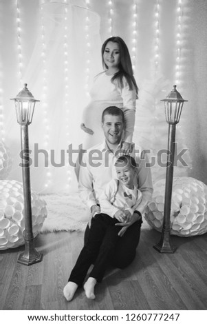 a little boy, pregnant woman and man near the lampposts and Christmas tree on the background of bright lights