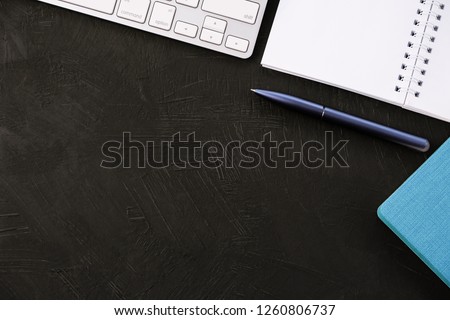 Business background: a keyboard, a blue pen and notebooks on a black desk top.