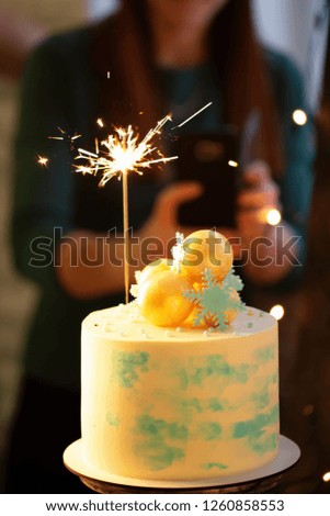 Decorated Christmas Cream Cake with burning sparkler, close up woman taking photo
