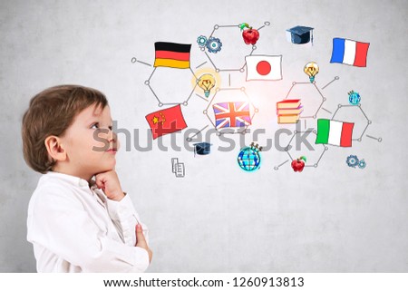Side view of adorable little boy in white shirt thinking standing near concrete wall with colorful international education sketch.