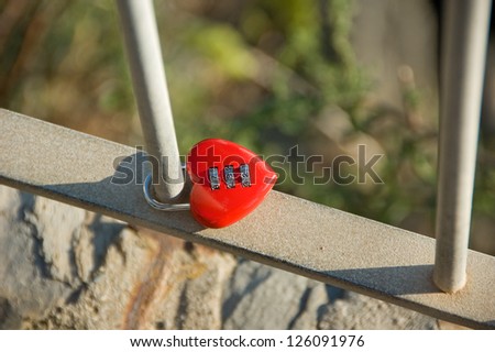 Red metal heart shaped lock with a code as a symbol of endless love on the metal grid in a park