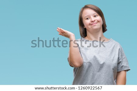 Young adult woman with down syndrome over isolated background smiling cheerful presenting and pointing with palm of hand looking at the camera.