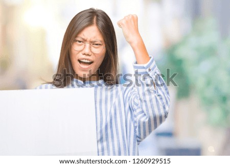 Young asian woman over isolated background holding blank banner annoyed and frustrated shouting with anger, crazy and yelling with raised hand, anger concept