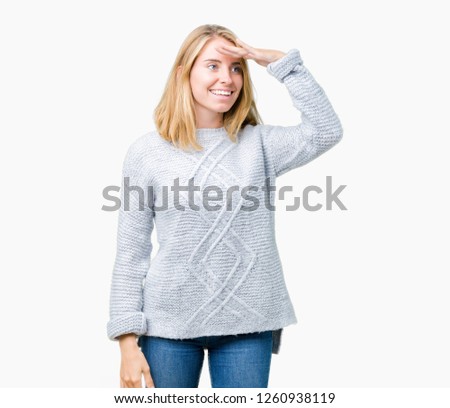 Beautiful young woman wearing winter sweater over isolated background very happy and smiling looking far away with hand over head. Searching concept.