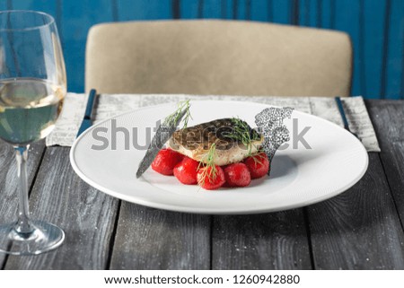 Tasty baked fish with cherry tomatoes, spices on dark rustic background. Grilled delicious fish. Diet and healthy food. Decorated by chef. Served in restaurant