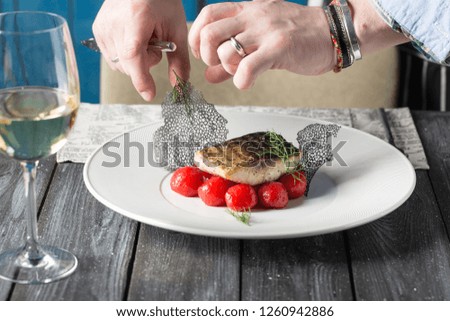 Tasty baked fish with cherry tomatoes, spices on dark rustic background. Grilled delicious fish. Diet and healthy food. Decorated by chef. Served in restaurant