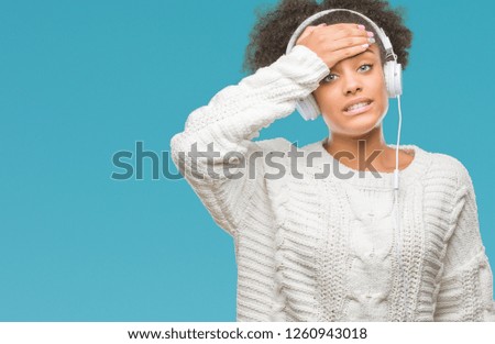 Young afro american woman wearing headphones over isolated background stressed with hand on head, shocked with shame and surprise face, angry and frustrated. Fear and upset for mistake.