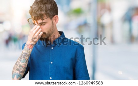Young handsome man wearing glasses over isolated background tired rubbing nose and eyes feeling fatigue and headache. Stress and frustration concept.