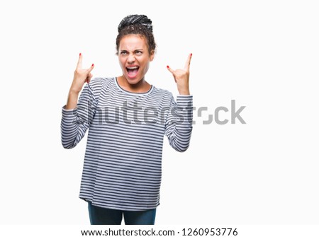Young braided hair african american girl wearing sweater over isolated background shouting with crazy expression doing rock symbol with hands up. Music star. Heavy concept.